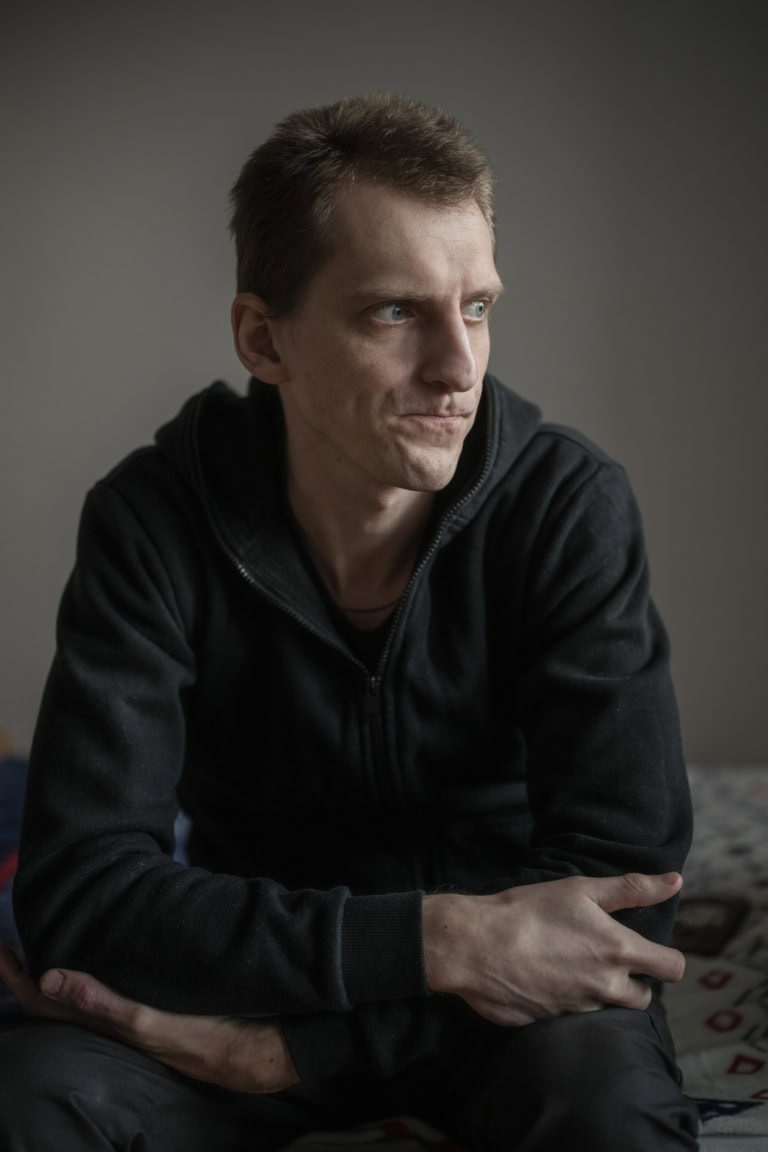 Portrait eines Mannes, ca 30 Jahre alt. Seine Arme sind verschränkt, er schaut angestrengt rechts aus dem Bild heraus.