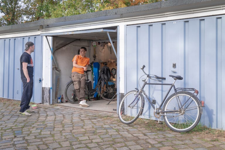 Tom (links) und ein Freund von ihm (rechts) stehen in ihrer Garage und quatschen, auf dem Garagenhof an der Wiesbadener Straße, 01159 Dresden. Sie nutzen diesen Raum hauptsächlich um an ihren Fahrrädern zu schrauben.