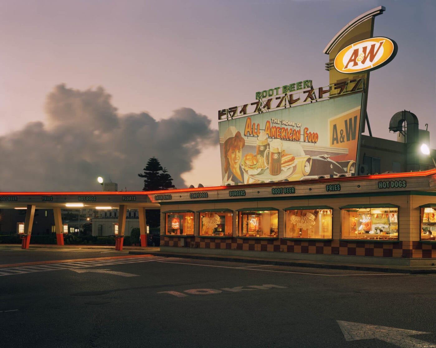 Ein nostalgischer Blick auf ein A&W-Restaurant in der Abenddämmerung, mit Neonlichtern und einem großen Vintage-Werbeschild für "All American Food." Die Szene fängt den Charme klassischer amerikanischer Diner ein. Dieses Bild wurde von einem Fotografie-Studenten während seines Fotografie Studiums aufgenommen.