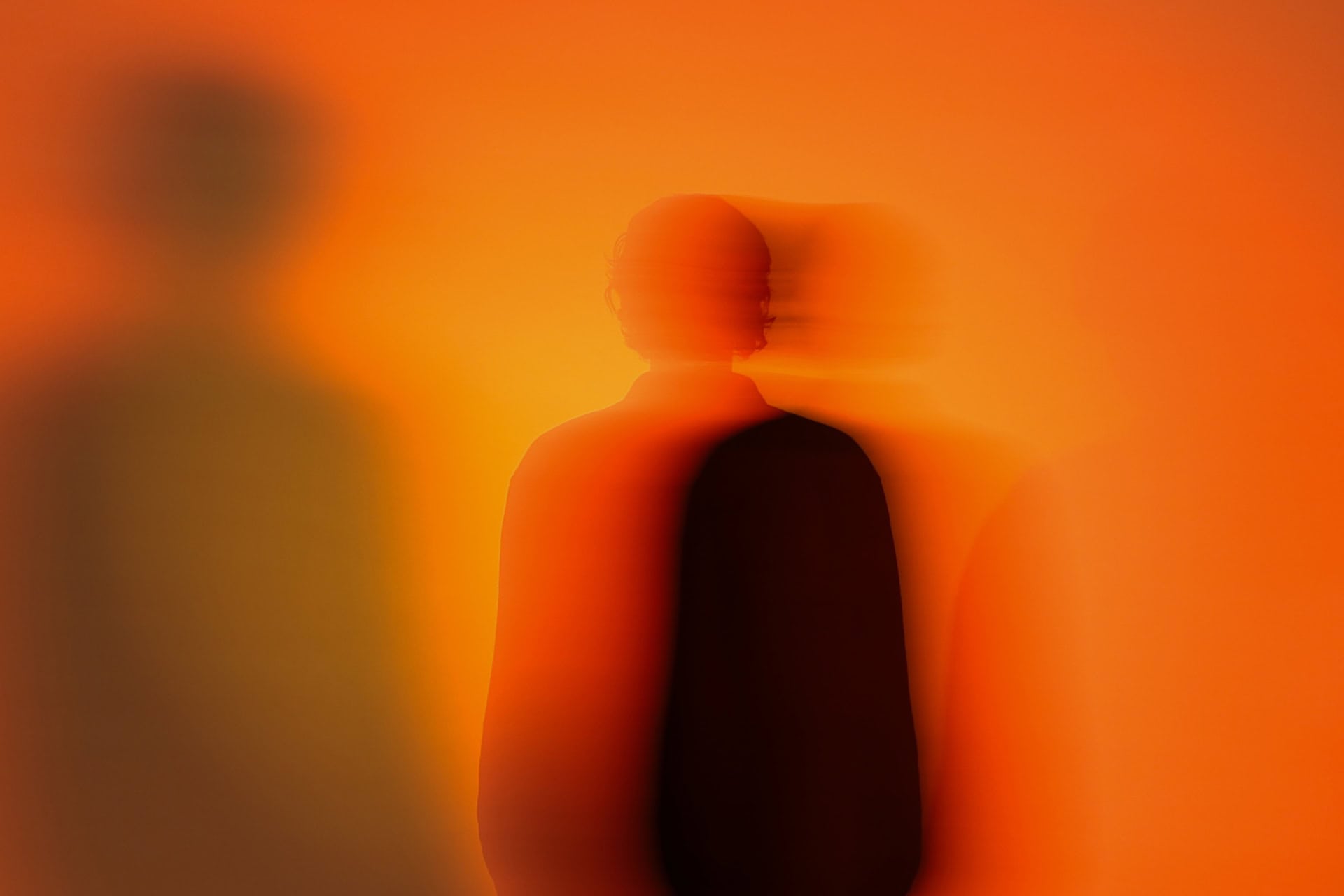 unscharfe Silhouette vom Oberkörper vor orangenem Hintergrund