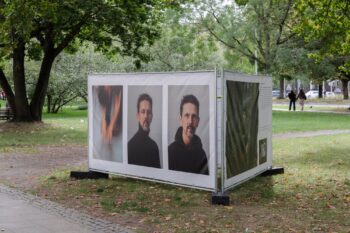 Weisse Ausstellungskabine mit Portraets unter Baeumen am Leibnizufer Hannover