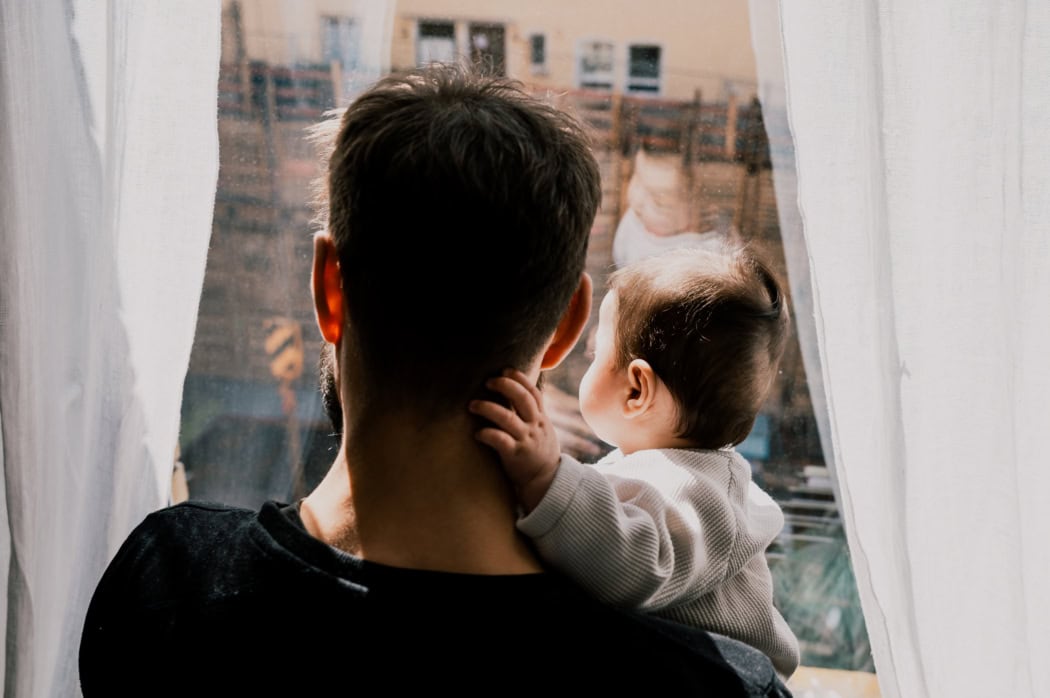 Vater hält Sohn auf dem Arm und schaut aus dem Fenster