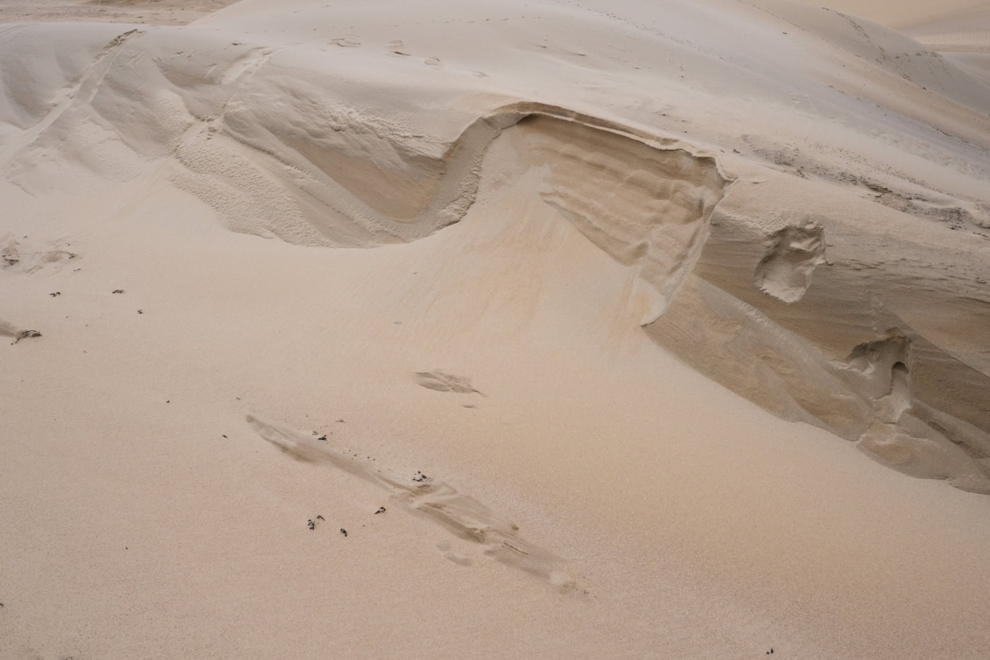 eine querformatige farbige Fotografie. Eine Wüstenlandschaft ist von oben fotografiert, mit einem leichten Sanhügel. Der Sandhügel ist in der Mitte des Bildes eingebrochen.