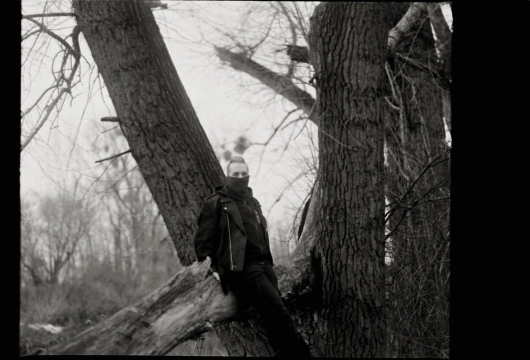 A man is sitting on a tree branch in the woods.