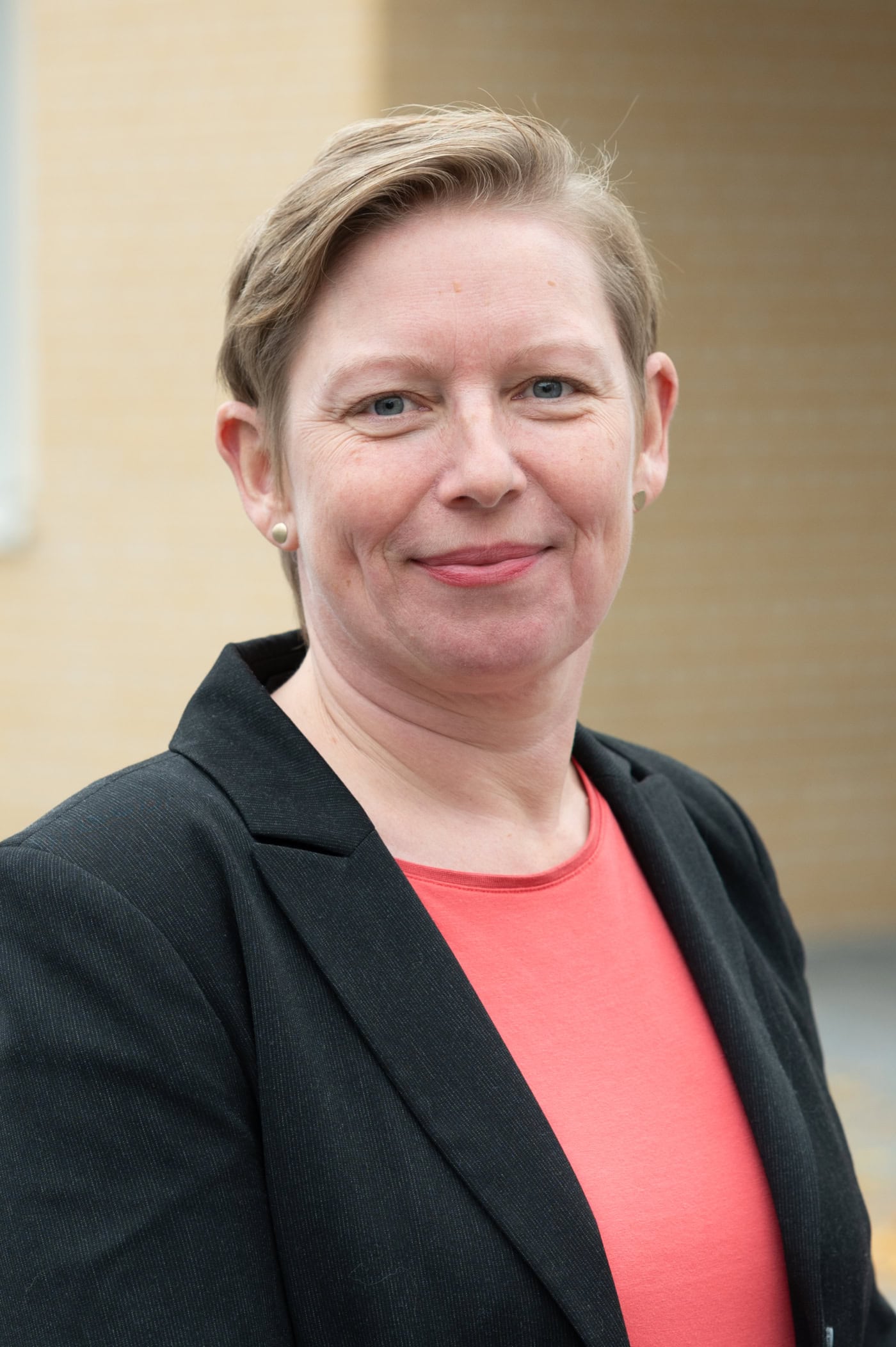 Auf dem Foto ist Karen Altmann, die Projektleiterin von New Work an der Hochschule Hannover zu sehen. Sie hat kurze, hellbraune Haare und schaut mit einem freundlichen Blick in die Kamera. Sie trägt einen schwarzen Blazer und ein apricotfarbenes TShirt.