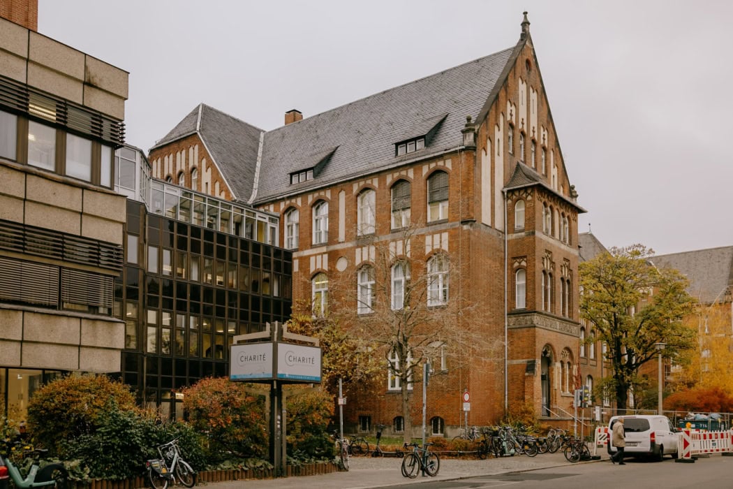 Historisches Gebäude der Charité Berlin mit Backsteinfassade und modernen Anbauten, umgeben von Fahrrädern und Herbstbäumen, aufgenommen an einem bewölkten Tag.