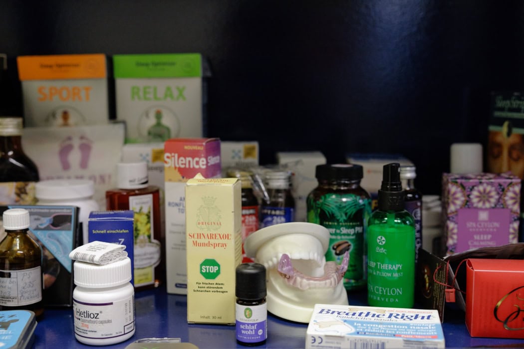 Sammlung verschiedener Produkte zur Schlafunterstützung und Schnarchreduktion, darunter Mundsprays, Schlafkapseln, Nasenpflaster und ätherische Öle. Im Vordergrund steht ein Zahnschutzmodell, umgeben von Verpackungen wie „Silence Schnarchspray“, „Schlaf wohl“-Öl und „Breathe Right“-Pflastern. Die Produkte sind in einer Mischung aus medizinischen und wellnessorientierten Artikeln arrangiert.