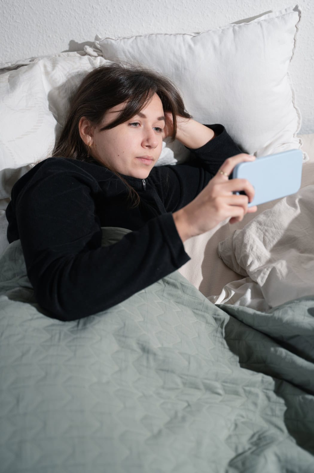 Portrait von Franzi. Sie liegt in ihrem Bett, hält ihr Smartphone mit einer hellblauen Hülle vor sich. Der Raum ist sehr hell ausgeleuchtet. Man sieht nur ihren Oberkörper, der Rest ist unter ihrer Bettdecke. Sie sieht gespannt auf den Bildschirm.