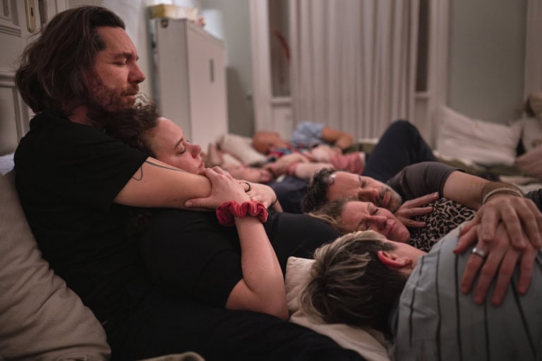 Gruppe von Menschen die Kuscheln / im Vordergrund zwei Menschen bei der der Mann die Frau im Arm hält / alle sind im Moment