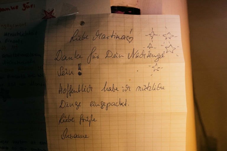 Das Bild zeigt eine handgeschriebene Notiz auf kariertem Papier mit Sternenzeichnungen und dem folgenden Text: „Liebe Martina, danke für dein Nachtengelein! Hoffentlich habe ich nützliche Dinge eingepackt. Liebe Grüße, Susanne.“ Die Notiz vermittelt Dankbarkeit und Fürsorge, möglicherweise im Zusammenhang mit einem Hilfspaket oder einer Geste der Unterstützung.
