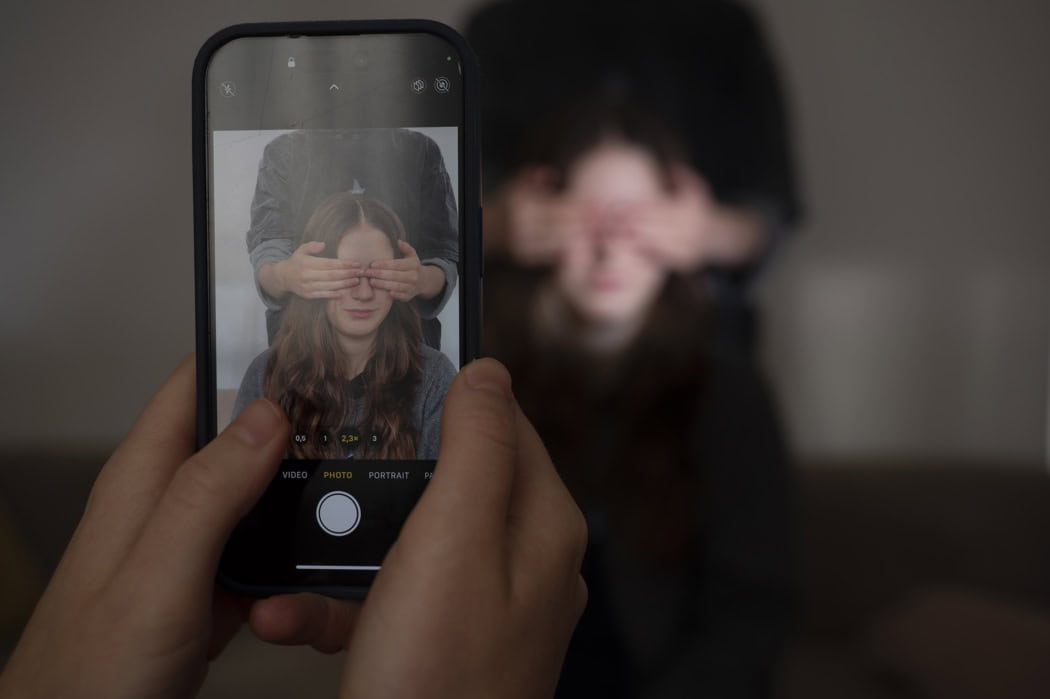 Foto eines Smartphone-Displays, auf dem einer Kidfluencerin die Augen verdeckt werden von einer anderen Person als Symbol für verloren gegangene Kindheit der Influencer.