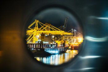 View through a hatch onto a yellow crane in the port of Rotterdam, photographed by Niklas Grüter.
