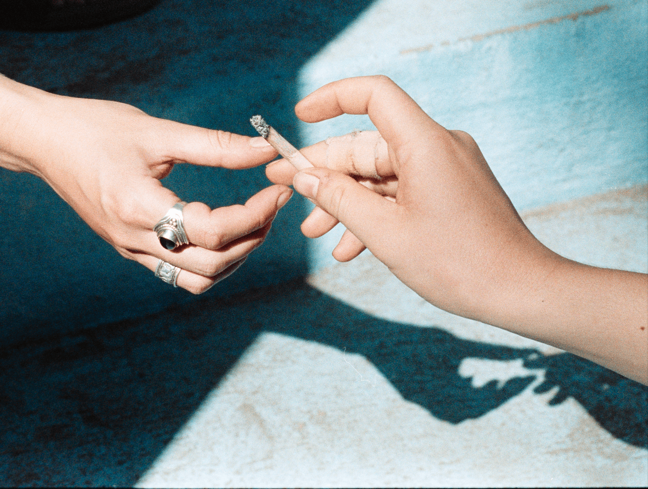 Zwei Hände teilen sich in antik anmutender Ästhetik eine Zigarette, Blitz, Editorial, Fotografie, Rauchen, Sucht