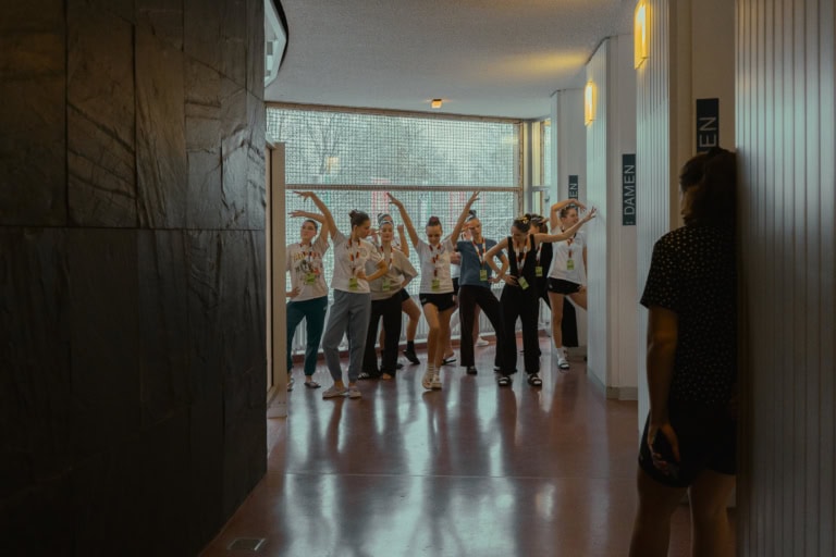 Eine Gruppe von Synchronschwimmerinnen vom SGS Hannover stehen in Alltagskleidung in einem Flur und üben eine Choreografie.