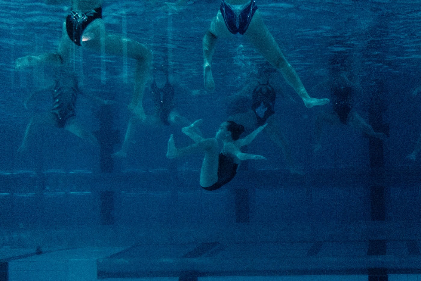 Mehrere Synchronschwimmerinnen befinden sich während der Aufführung einer Choreografie in einem Schwimmbecken. Die Synchronschwimmerinnen sind teilweise oder komplett Unterwasser zu sehen.