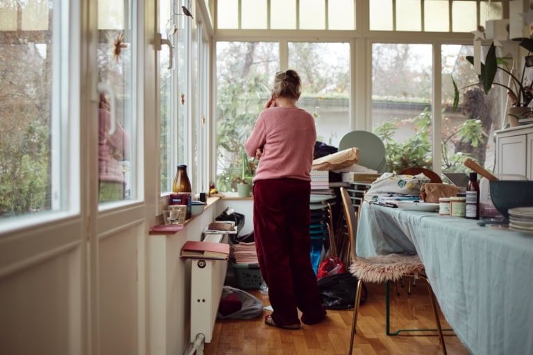 Eine Frau telefoniert in einem lichtdurchfluteten Raum, steht allerdings mit dem Rücken zu uns.