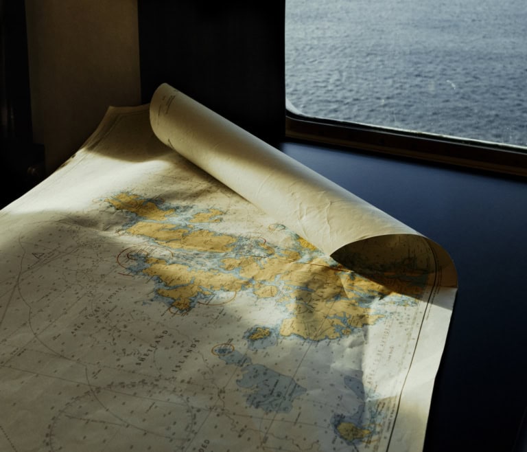 Auf einem schwarzen Tisch an Bord der MS Norröna liegt eine Seekarte. Darauf zu sehen sind die Färöer-Inseln, Island, Dänemark und das Nordmeer.