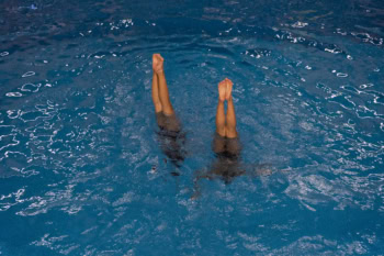 Zwei Synchronschwimmerinnen vom SGS Hannover stehen senkrecht und kopfüber in einem Schwimmbecken. Dabei sind nur noch ihre Beine über der Wasseroberfläche zu sehen.