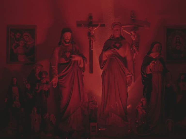 Eine Sammlung religiöser Statuen und Ikonen, darunter Jesus-Statuen und Kreuze, die in rotes Licht getaucht sind, in einem Raum eines Wahrsagers in Deutschland.