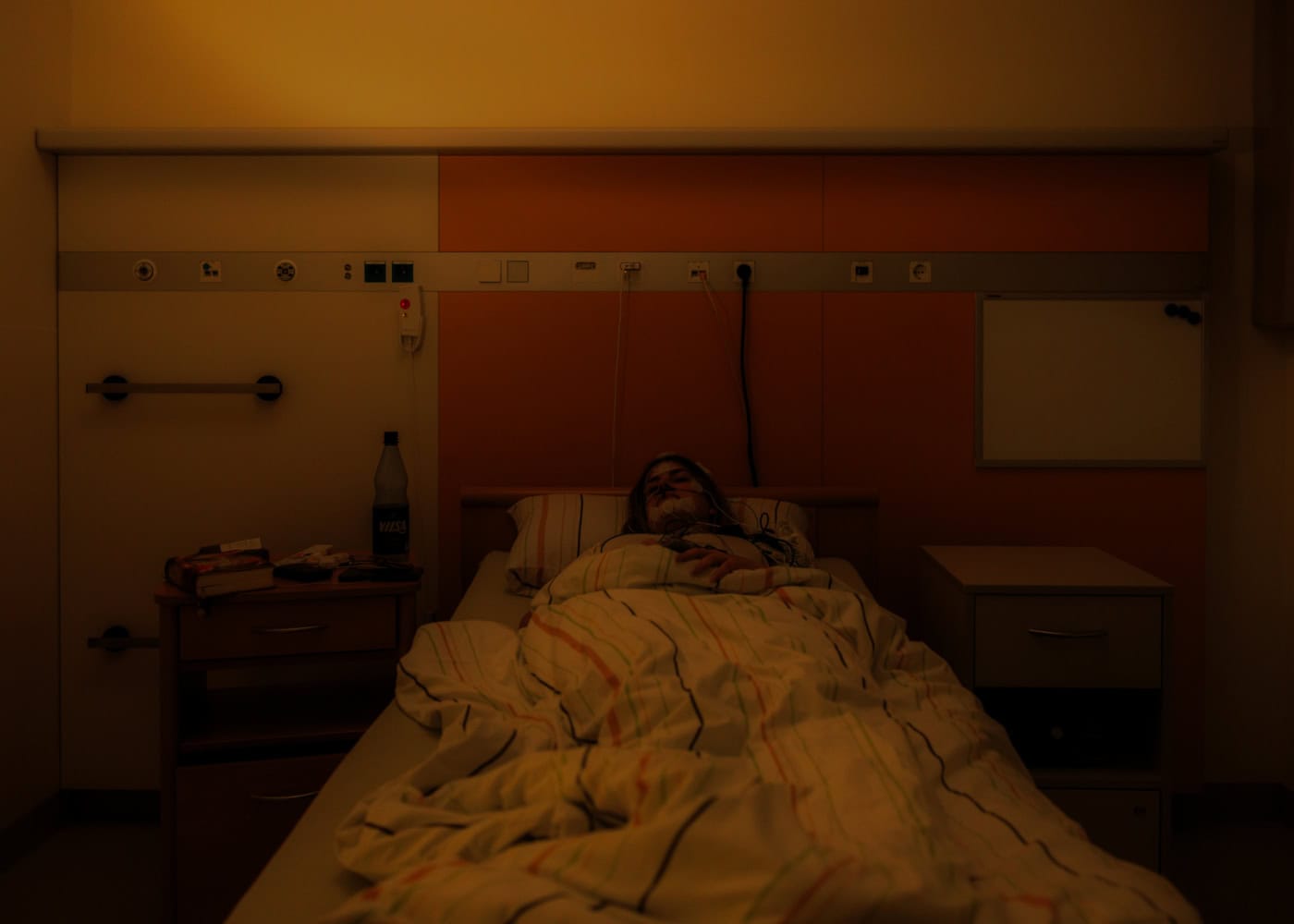 Sommer schläft in dem Bett des Schlaflabors. Man kann sehen, dass sie am ganzen Kopf verkabelt ist. Das Licht ist gedimmt, sodass man sie nur dezent erkennen kann.