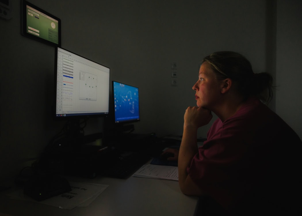 Die Krankenschwester schaut sich Sommers Werte auf dem Computer an. Der Bildschirm leuchtet ihr ins Gesicht, während der Raum dunkel wirkt.