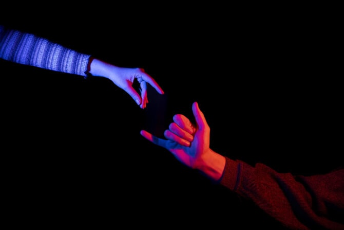 Eine blau und eine rot beleuchtete Hand strecken sich vor schwarzem Hintergrund einander entgegen – Gebärdensprache und Gehörlosigkeit