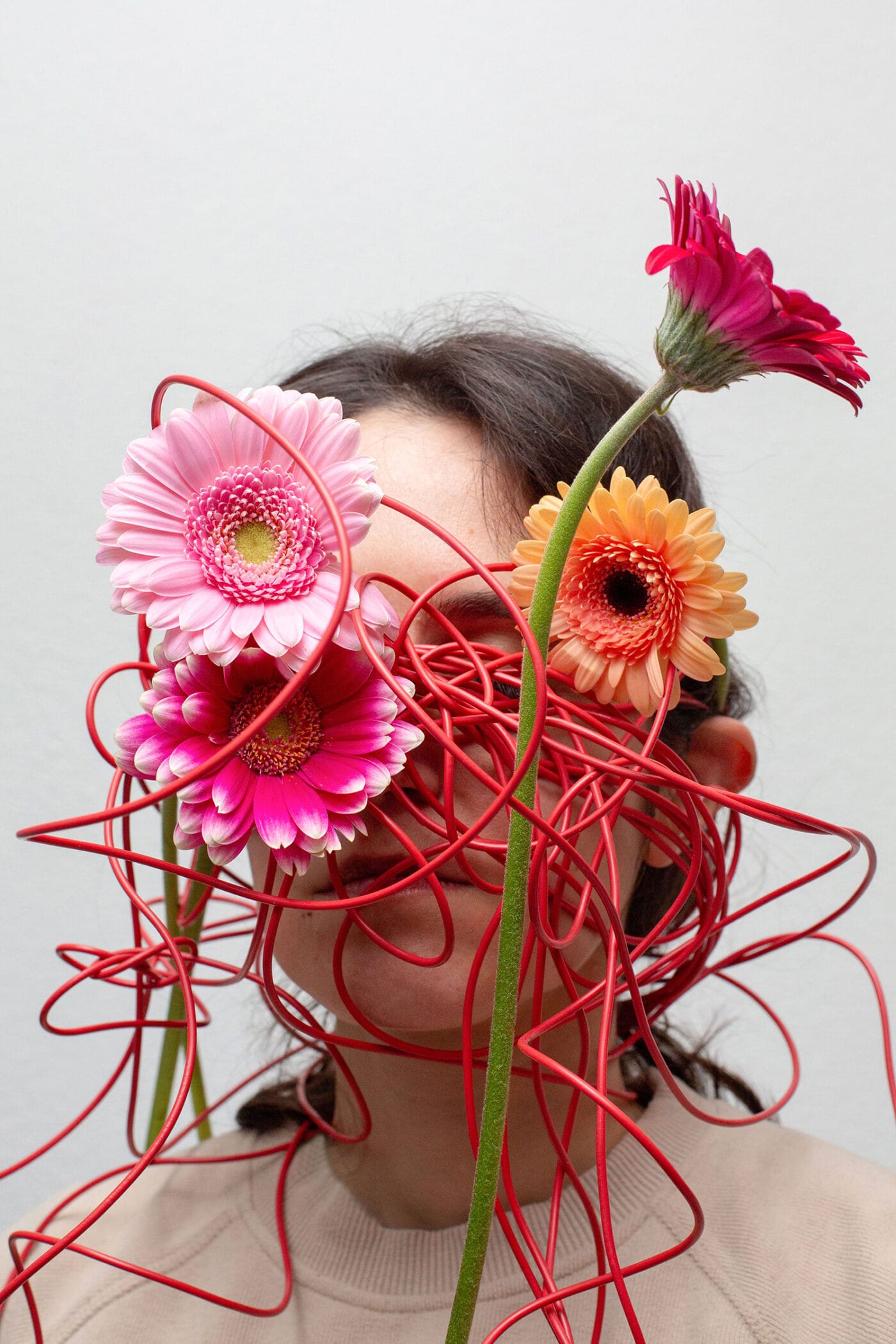 Rötliche Plastikblumen sind verknäuelt vor dem Gesicht einer jungen Frau platziert, symbolisch für die Unruhe im Kopf.